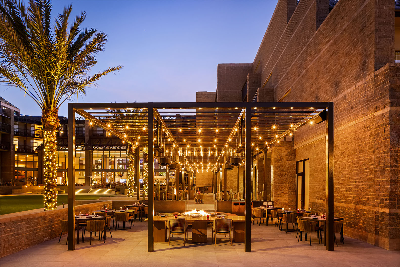 Spacious outdoor dining area with a pergola and fairy lights, framed by palm trees and stylish seating arrangements.