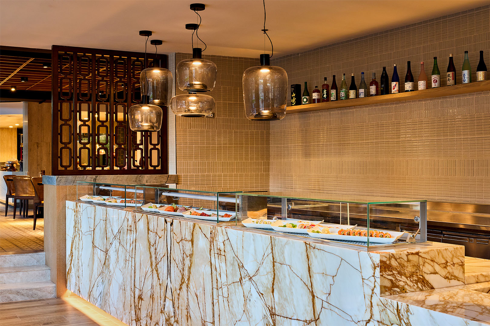 Sleek sushi counter with striking marble finish, modern glass pendant lights, and a display of Japanese sake bottles.